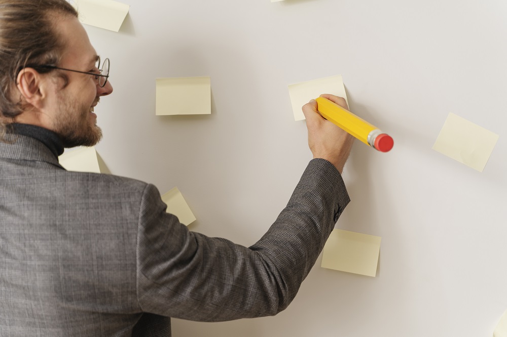 Hombre escribe en post it sobre plantilla de Business Model Canvas